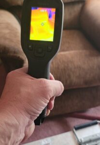 Hand holding a thermal camera reading 156 degrees beside a couch