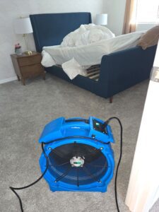 Blue air mover fan in a bedroom with a stripped bed
